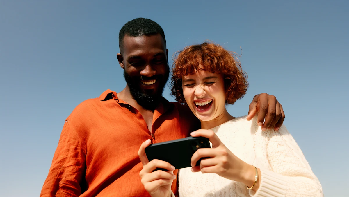 Un couple qui rit en regardant un téléphone, sous un ciel bleu