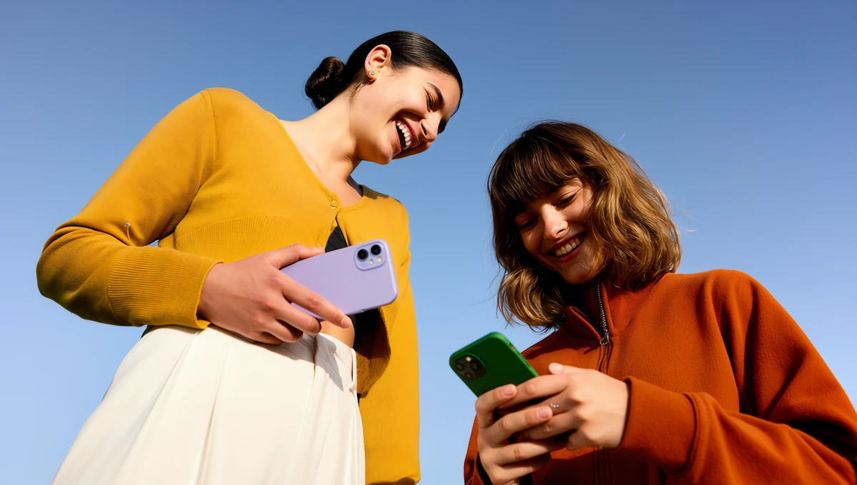 Deux femmes souriantes qui regardent leurs téléphones, sous un ciel bleu