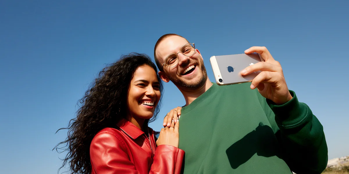 Un couple souriant qui prend un égoportrait avec un iPhone, sous un ciel bleu